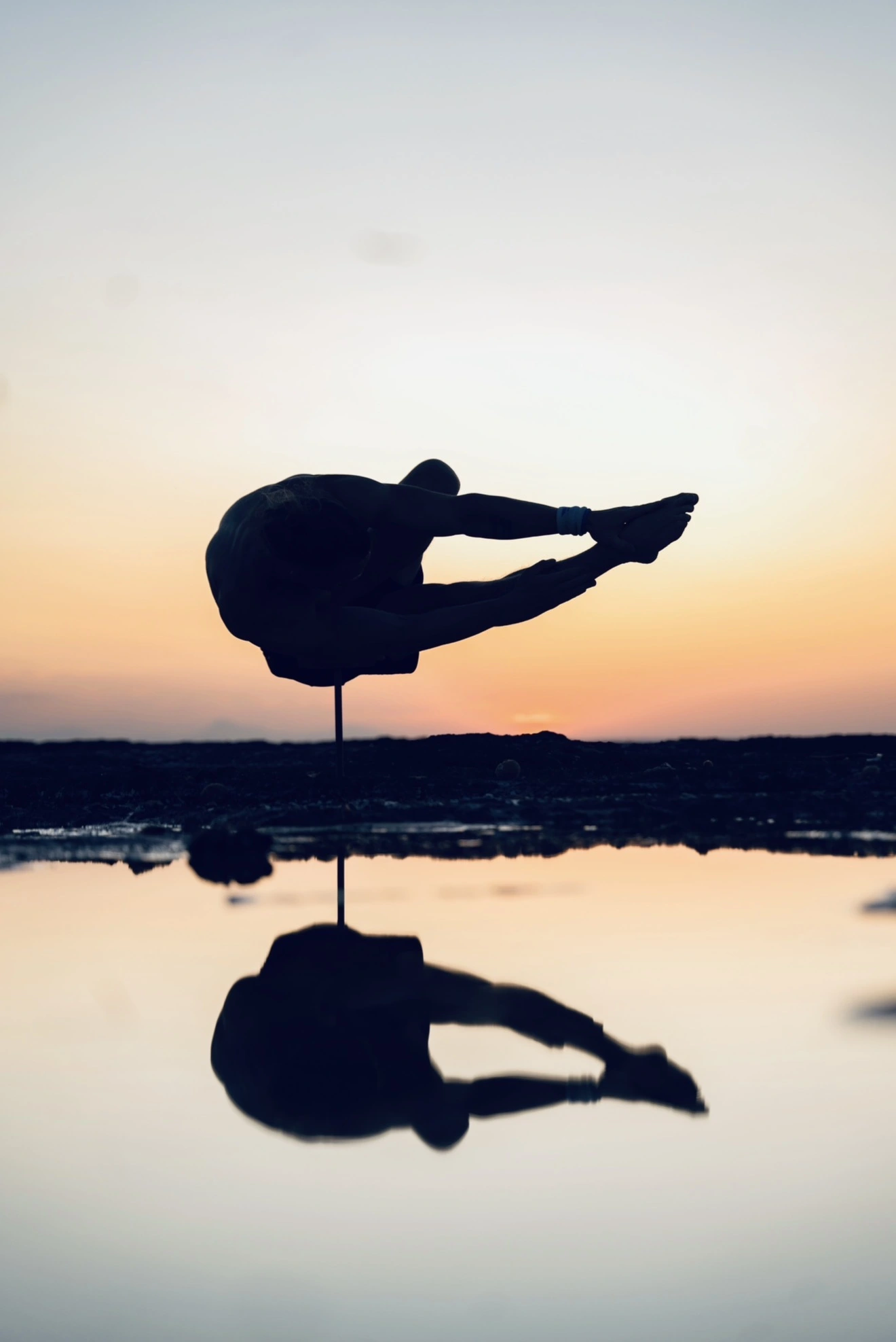 Yoga practitioner balancing in silhouette against a sunset sky